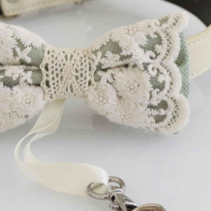 Close-up of sage green lace ring bearer dog bow tie showing floral embroidered lace details, decorative center wrap, and attached wedding ring holder ribbon