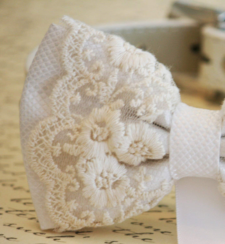 White lace ring bearer dog bow tie close-up with embroidered floral lace overlay, textured center band, and attached wedding ring holder ribbon