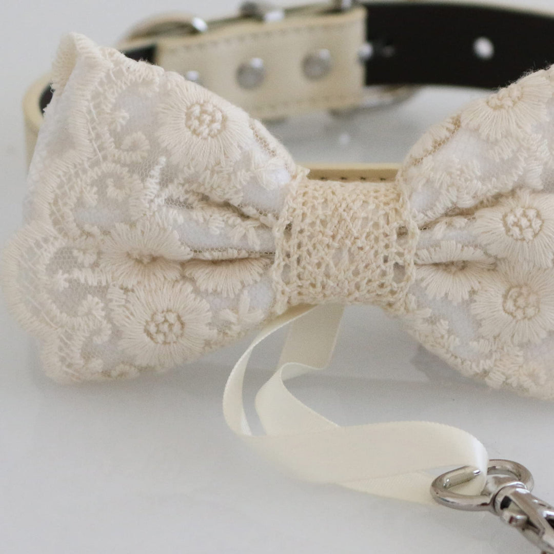 Close-up detail of white lace ring bearer dog bow tie with floral embroidered lace overlay, attached wedding ring holder ribbon, decorative ring charm, and adjustable vegan leather collar