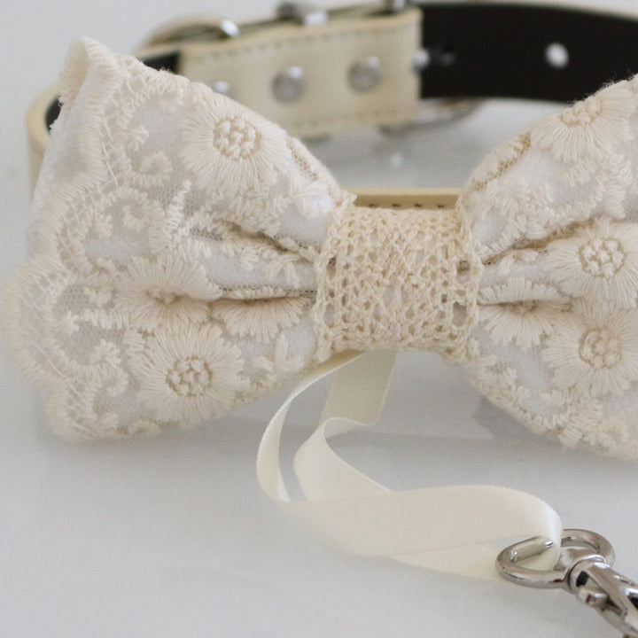 Close-up detail of white lace ring bearer dog bow tie with floral embroidered lace overlay, attached wedding ring holder ribbon, decorative ring charm, and adjustable vegan leather collar