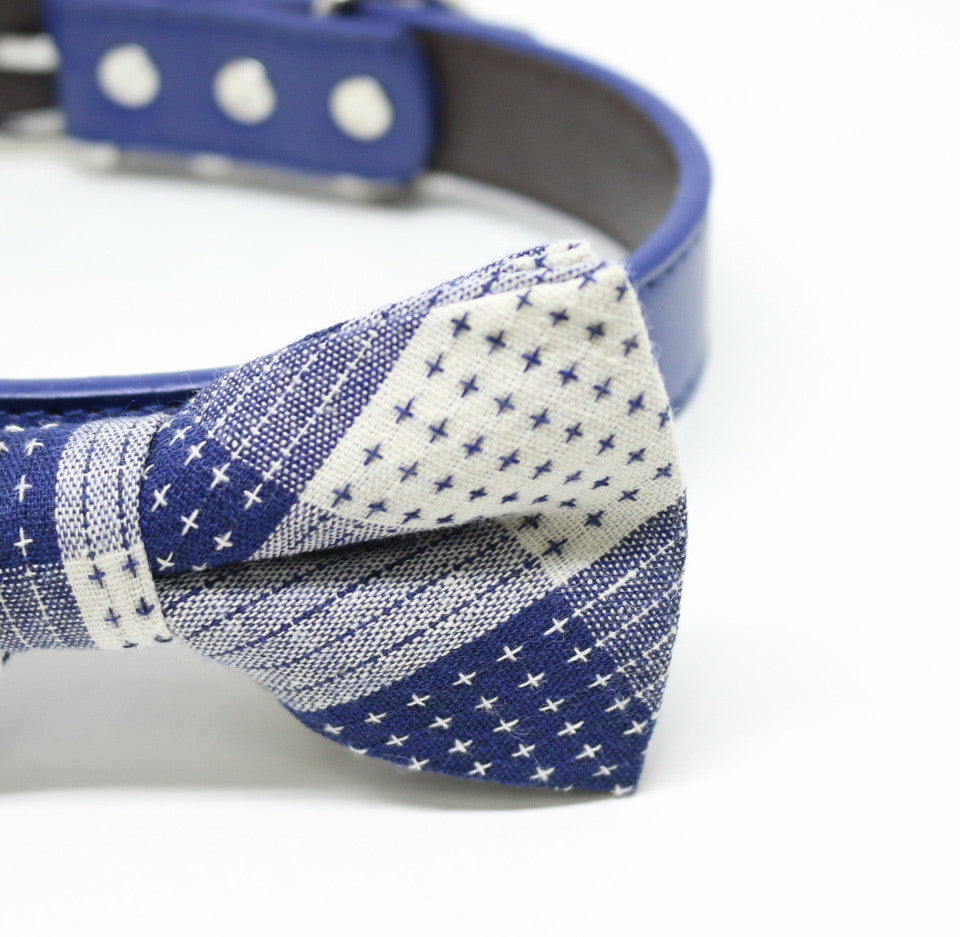 Close-up of blue and white patchwork dog bow tie featuring mixed stripe and cross-stitch patterns on a blue vegan leather collar