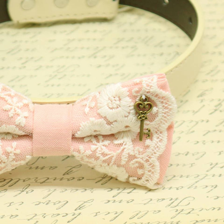 Blush pink lace dog bow tie collar close-up showing antique bronze key charm, floral embroidered lace details, and soft pink fabric accents