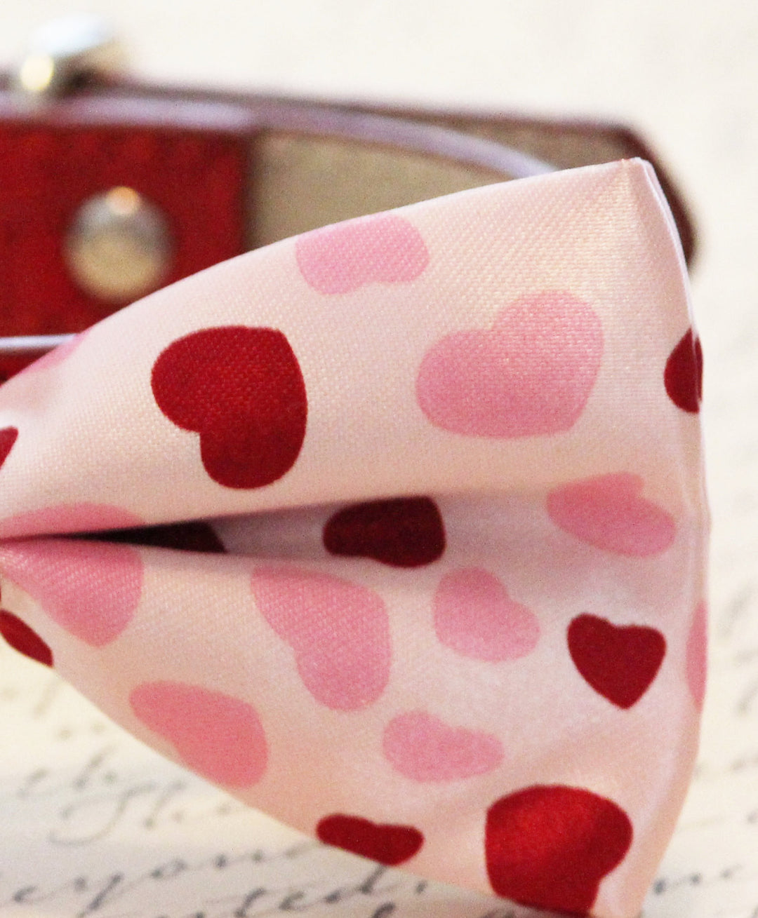 Close-up of pink dog bow tie with red and pink heart pattern on satin fabric.