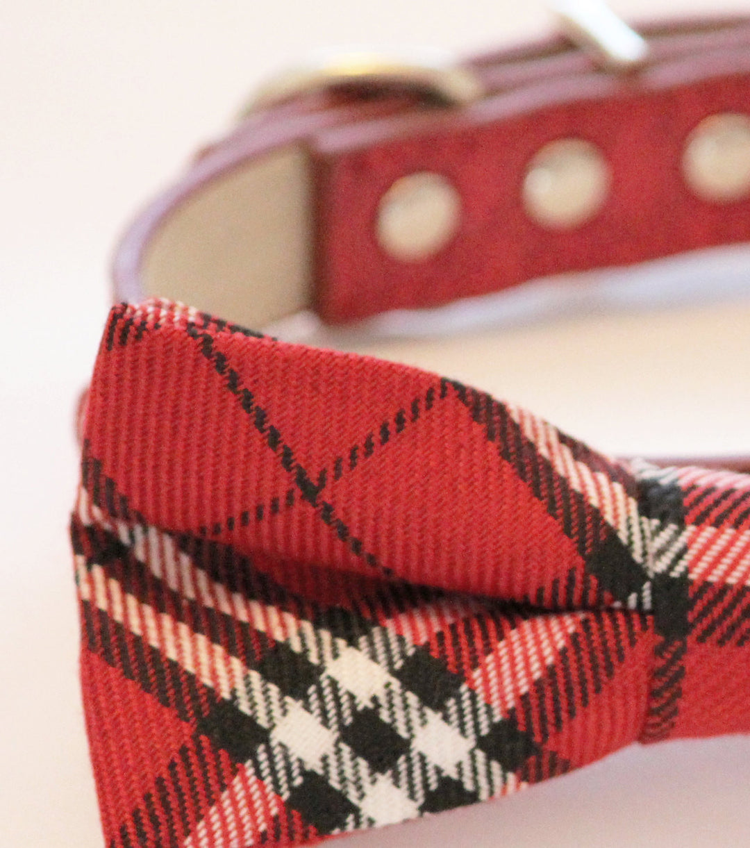 Close-up detail of a red tartan plaid dog bow tie with black and white pattern accents.