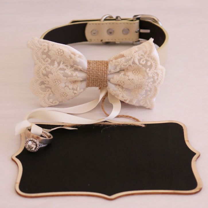 White lace ring bearer dog bow tie collar featuring floral embroidered lace, burlap center detail, attached wedding ring holder ribbon, and decorative ring next to a blank wedding signboard backdrop